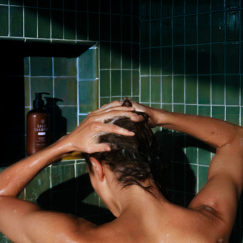 Basic Shampoo REVIVE bottle in a green-tiled shower room with a lady cleansing her hair